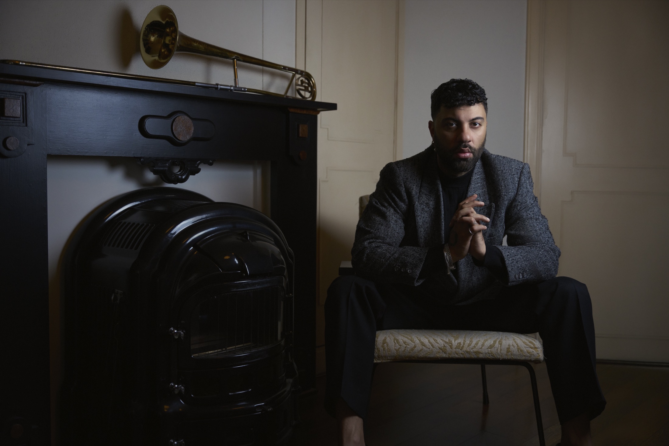 Efe Erdem seated beside a fireplace, with a trombone resting above it